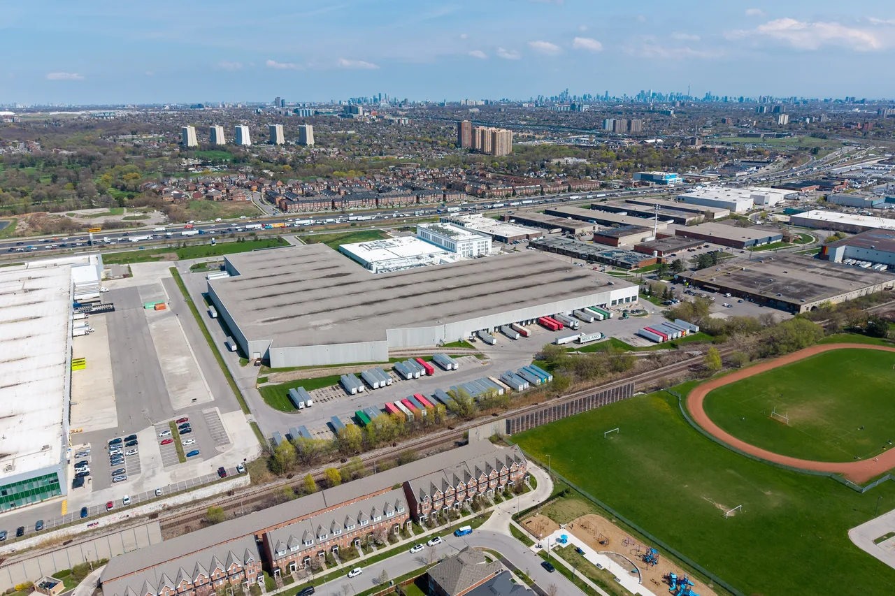 Aerial view of a large industrial building beside a rail line with the Toronto skyline in the distance